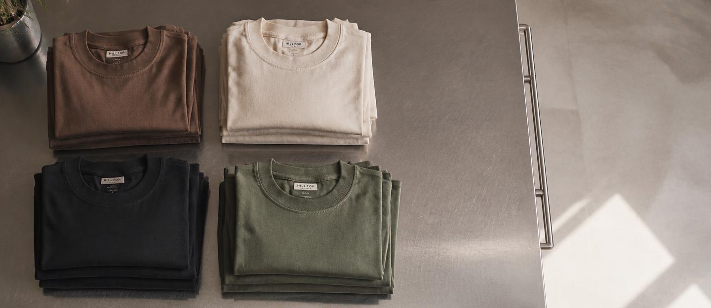 Folded heavyweight cotton t-shirts on a stainless steel kitchen prep table